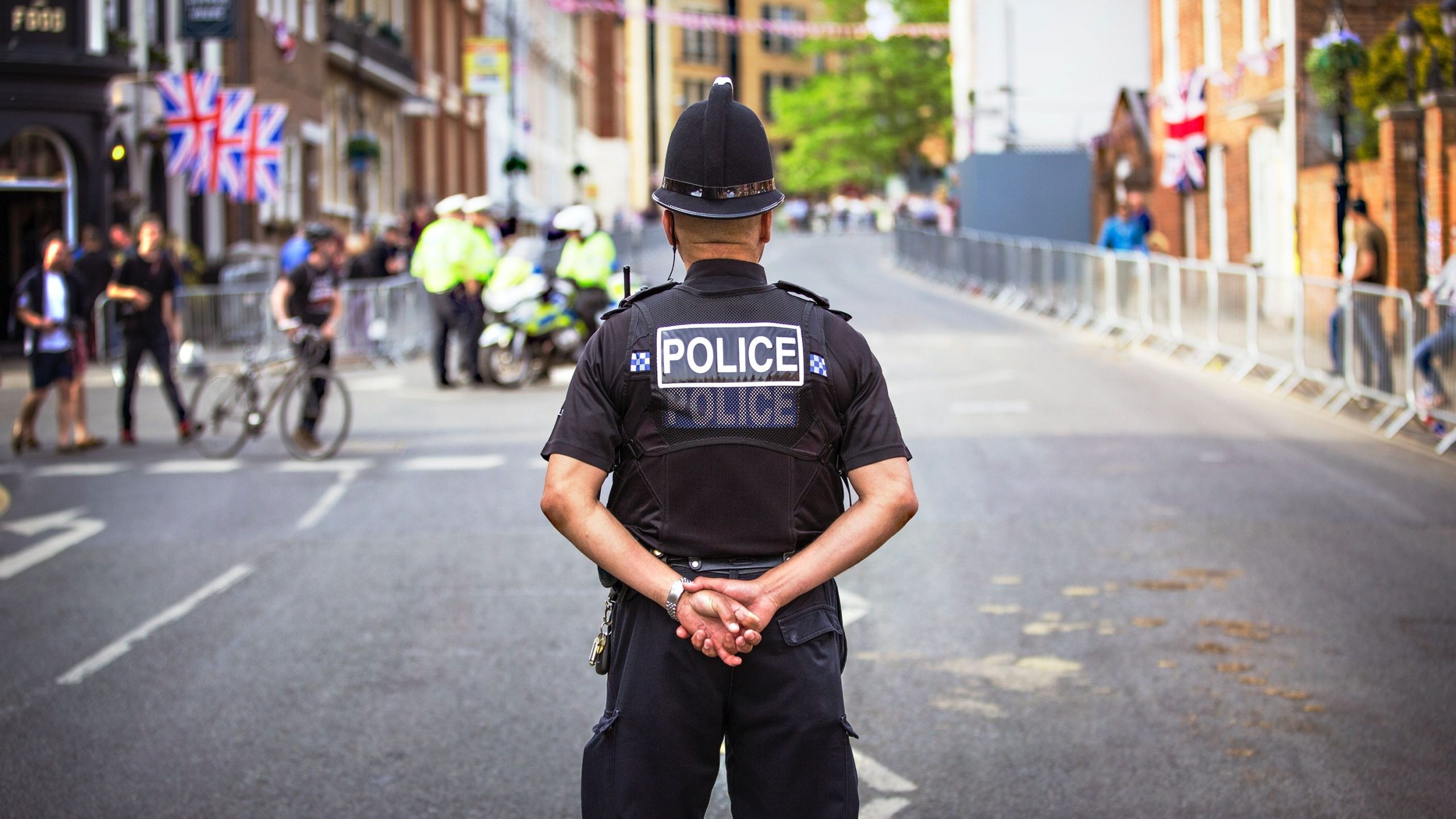 A U.K. policeman seen from behind stands in the middle of road