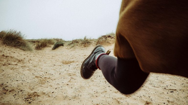 Close up of a person's leg as they run across a sand dune.